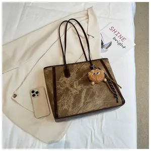 Detailed view of tote bag with vintage brown texture, leather straps, and plush charm