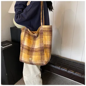 Detail of yellow wool plaid tote bag featuring a handmade metal plate and rich texture