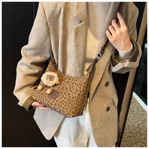Close-up of leopard print crossbody bag with leather strap and plush sheep charm on model