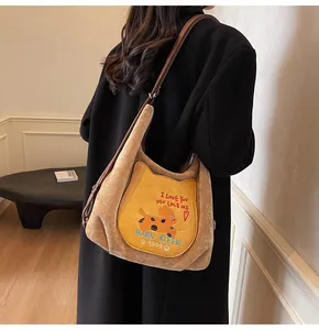 Détail d'un sac cabas en daim kaki avec poche chat jaune et broderie porté par un mannequin