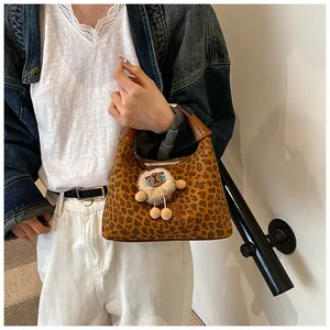 Close-up of a leopard print hobo bag with a plush lamb charm and brown leather handles
