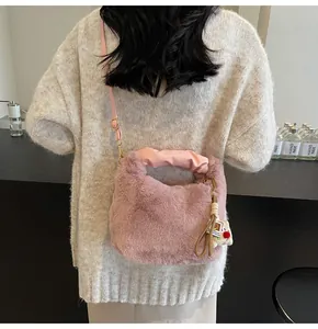Rosa Plüsch-Eimertasche mit Ledergriff und Anhänger auf beigem Strickpullover