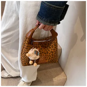 Detail of leopard print handbag with leather handle and plush charm hanging on the side