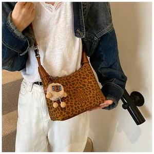 Detail of leopard print crossbody bag with leather trim and plush animal keychain
