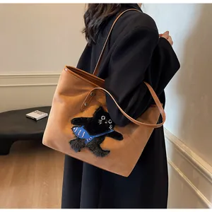 Detail of a brown tote bag featuring unique black cat embroidery with a blue fish accent