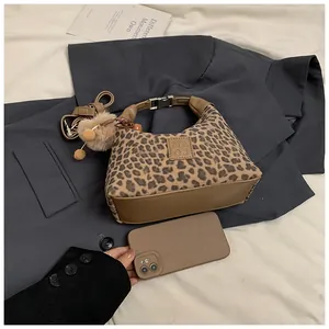 Detail of leopard print handbag featuring brown leather trim and plush ball pendant