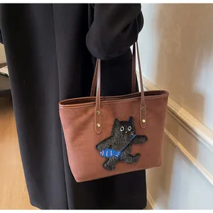 Close-up of brown suede tote bag featuring a cute cat patch and durable leather straps