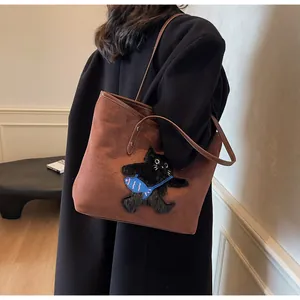 Detail shot of brown suede tote bag with a cute black cat patch shown on a model's shoulder