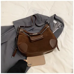 Close-up of brown suede crescent bag on a grey blazer with silver chain and mini pouch