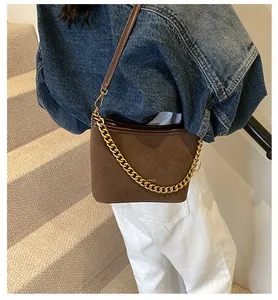 Detail of dark brown suede shoulder bag featuring a gold chain strap and BAGS logo
