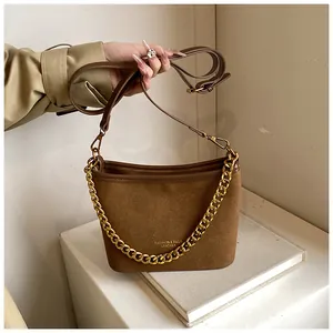Detail of brown suede bucket bag featuring chunky gold chain and leather shoulder strap