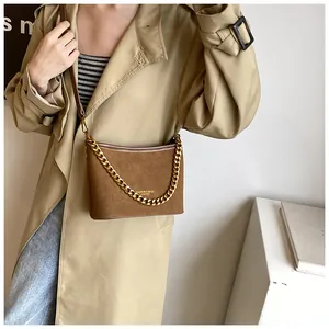 Detail of brown suede bucket bag featuring gold chain strap and embossed leather logo