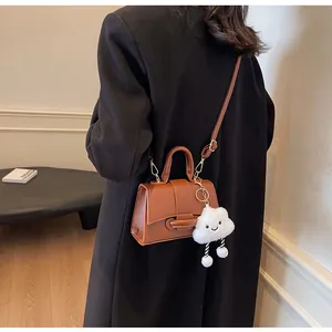 Brown leather crossbody bag detail with a cute plush cloud charm on a black coat