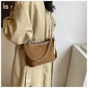 Detail of a brown suede crossbody bag featuring a golden chain and fashion metal logo