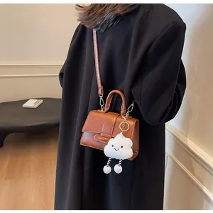 Brown vintage flap shoulder bag with cute white cloud pendant worn on black coat