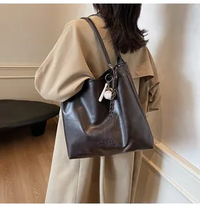 Detail of dark brown faux leather tote bag featuring a sports-themed charm and logo