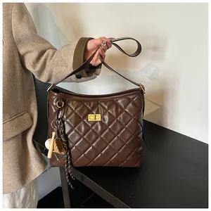 Détail du sac à bandoulière matelassé marron foncé avec fermoir doré et breloque baseball