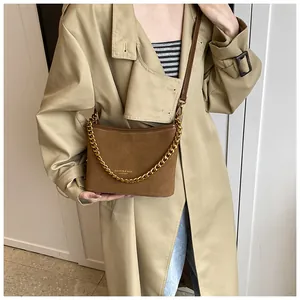Close-up of brown suede crossbody bag with gold chain strap on a khaki trench coat