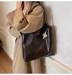 Detail of mocha brown tote bag featuring M.SHAN logo and baseball charm on beige coat