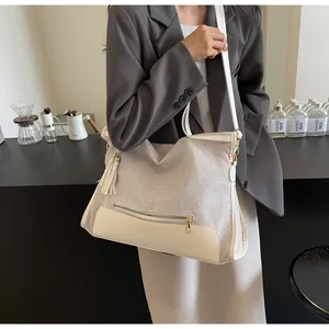 Detail of canvas tote bag showing white fringe tassel and external metal zipper pocket
