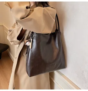 Detail of mocha tote bag with H.SHAN logo and baseball charm on leather surface