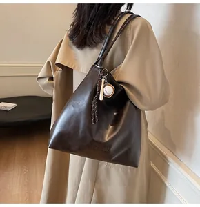 Detail of dark brown leather tote bag with brand embossing and creative baseball pendant
