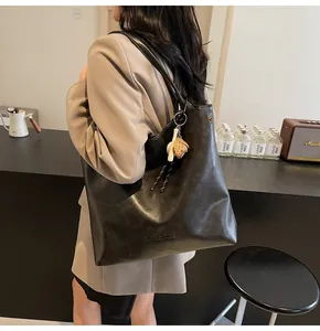Chic black large tote bag with baseball pendant charm worn by model in cafe setting