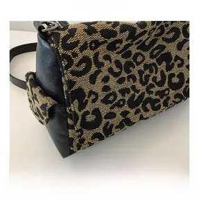 Detail shot of leopard print canvas bag with black leather trim and functional side pocket