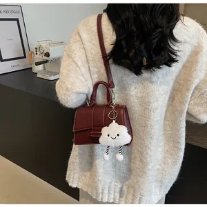 Detail of burgundy leather mini bag with whimsical white cloud plush charm accessory