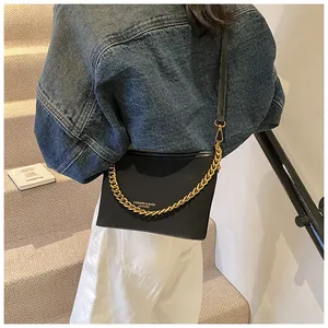 Detail of minimalist black leather bucket bag featuring a chunky gold chain strap and logo