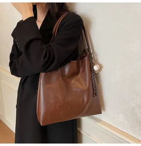 Detail of mocha brown tote bag with baseball charm and shoulder strap on model
