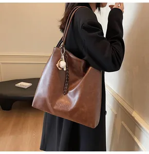 Detail view of mocha brown tote bag featuring baseball charm and H.SHAN logo engraving