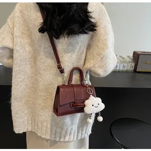 Detail of dark red leather crossbody bag with white plush charm and adjustable strap