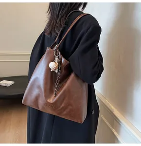 Detail of mocha brown tote bag with baseball charm and H.SHAN branding on soft leather