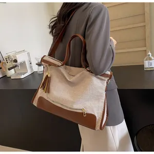 Détail du sac cabas en toile et cuir marron avec gland à franges porté par un mannequin