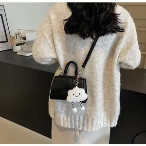Close-up of black leather crossbody bag with a cute cloud plush charm on a knit sweater