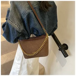 Detail of dark brown suede bucket bag featuring chunky gold chain and long shoulder strap