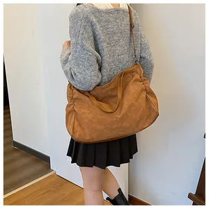 Detail of a large brown suede tote bag with pleated side design worn on the shoulder