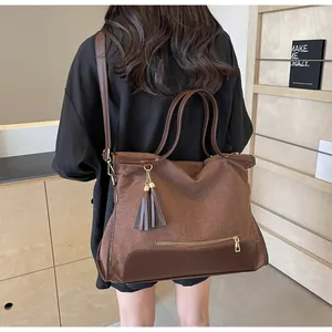 Detailed view of brown canvas tote bag with leather trim and decorative double tassels
