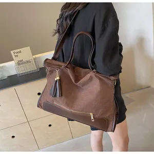 Détail d'un grand sac cabas tissé marron avec bordure en cuir et pompon sur un modèle