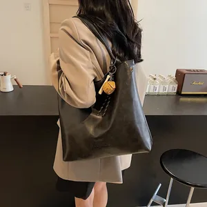 Classic black leather tote bag with long straps and yellow strawberry charm on display