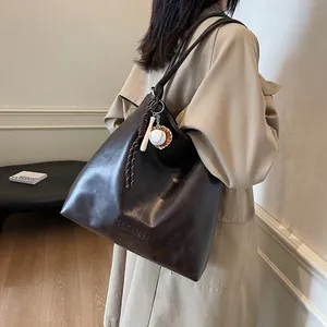 Mocha brown faux leather tote bag with a baseball bat charm shown on a trench coat