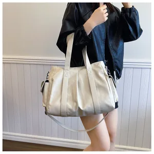 Detail of a large beige PU leather tote bag with side pockets on a model in a black jacket
