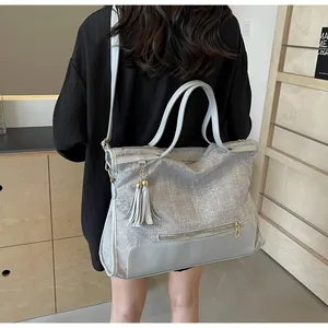 Grand sac cabas gris avec pompon et poche zippée porté par un mannequin en intérieur