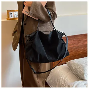 Detail of a black minimalist canvas tote bag with slim leather straps on a female shoulder