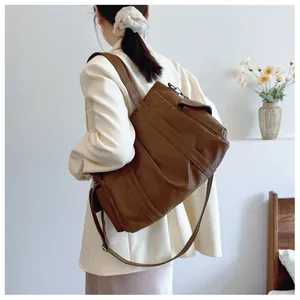 Detail of a large brown leather tote bag with wide shoulder strap and adjustable crossbody belt