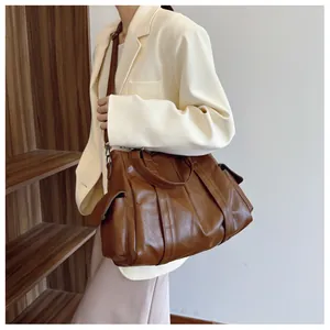 Detail of a large brown tote bag with adjustable shoulder straps and side flap pockets