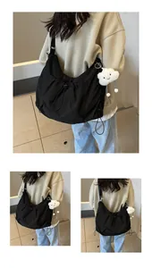 Detail view of large black crossbody bag featuring a soft white plush cloud charm accessory