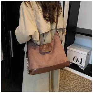 Detail of dark brown faux suede and leather shoulder bag with embossed logo and metal chain