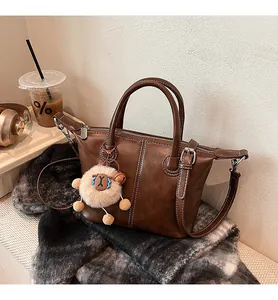 Detail of brown tote bag featuring white contrast stitching and a fuzzy white charm